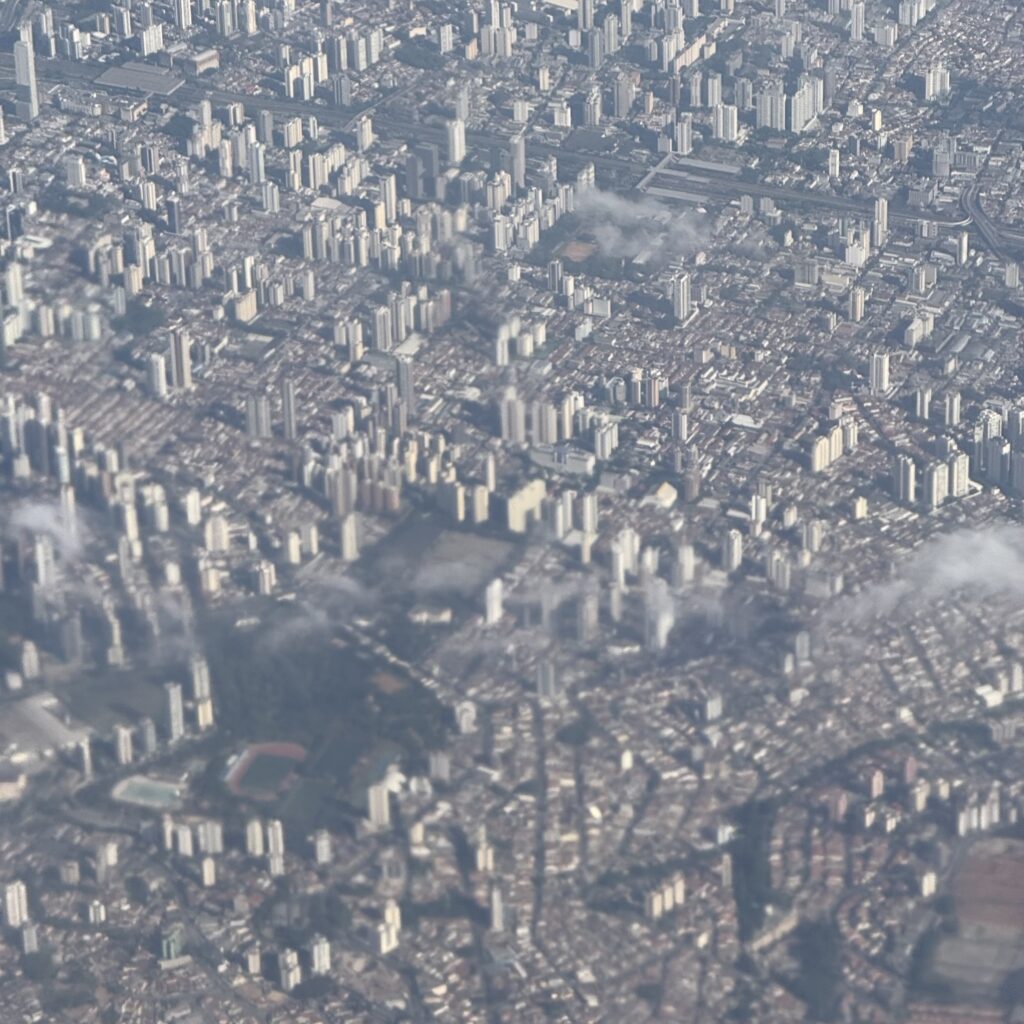 Aerial view of a densely built city - São Paulo in Brazil - with numerous high-rise towers, low-rise neighborhoods, roads, sports fields, and haze.