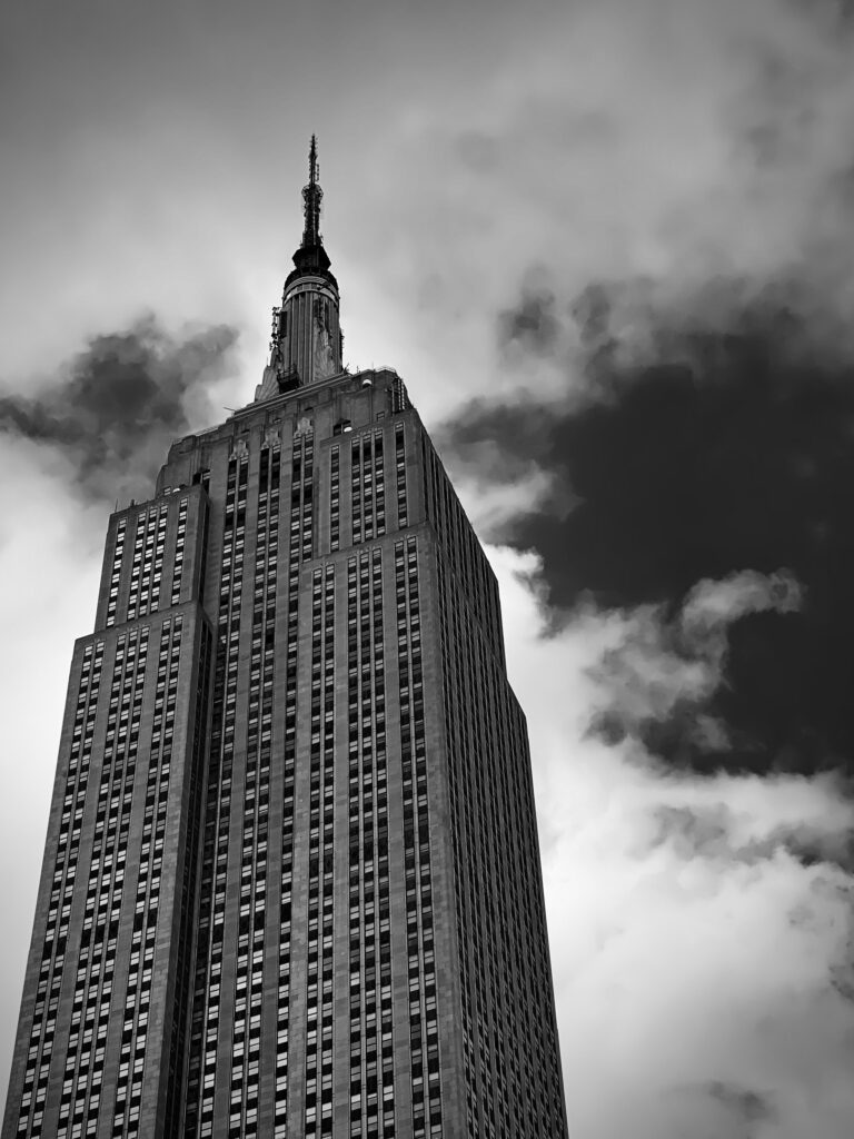 Black-and-white upward view of the Empire State Building in Manhattan, New York, against dramatic clouds.